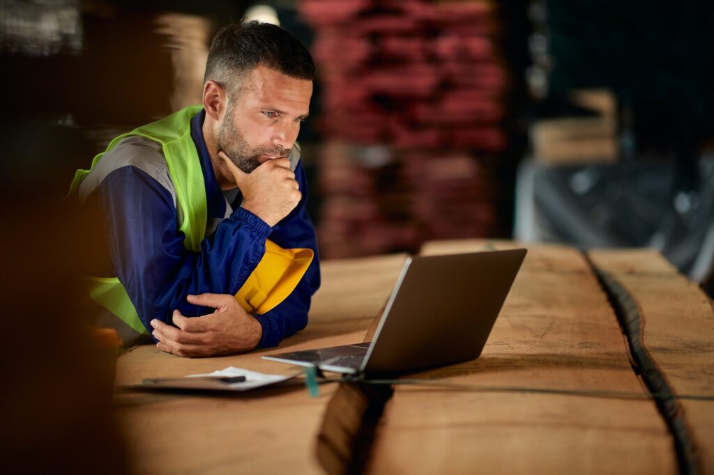 Pensive foreman reading an e-mail on laptop while working in a warehouse.